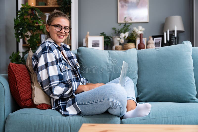 Young female freelancer in casual clothes sitting on comfortable couch and working remotely on laptop. Woman copyright writer or web developer work at home sitting on sofa enjoying her freedom. Young female freelancer in casual clothes sitting on comfortable couch and working remotely on laptop. Woman copyright writer or web developer work at home sitting on sofa enjoying her freedom