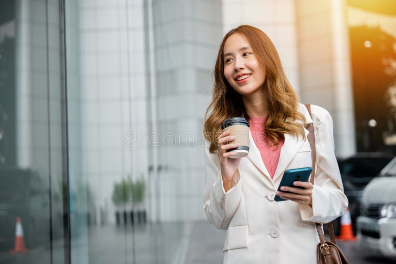 A smart businesswoman stays connected on the go with her smartphone and a cup of coffee. She is navigating the busy city with ease. A smart businesswoman stays connected on the go with her smartphone and a cup of coffee. She is navigating the busy city with ease.