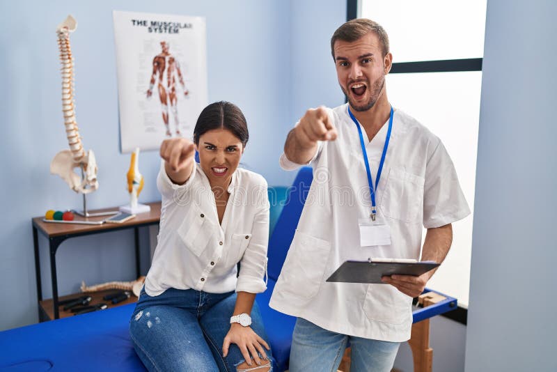 Young hispanic woman at physiotherapist appointment pointing displeased and frustrated to the camera, angry and furious with you. Young hispanic woman at physiotherapist appointment pointing displeased and frustrated to the camera, angry and furious with you