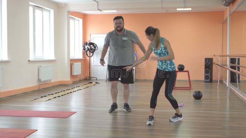 νεαρή κοπέλα γυμνάστρια από τον Καύκασο εκπαιδεύει έναν άντρα με μούσι σε γυμναστήριο για να καίει λίπος. προβλήματα υπερβολικού β