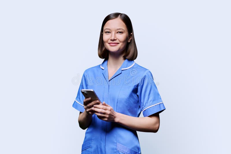 Smiling young female nurse using smartphone, looking at camera on white studio background. Mobile apps applications, technologies in medical services, health, professional assistance, medical care. Smiling young female nurse using smartphone, looking at camera on white studio background. Mobile apps applications, technologies in medical services, health, professional assistance, medical care