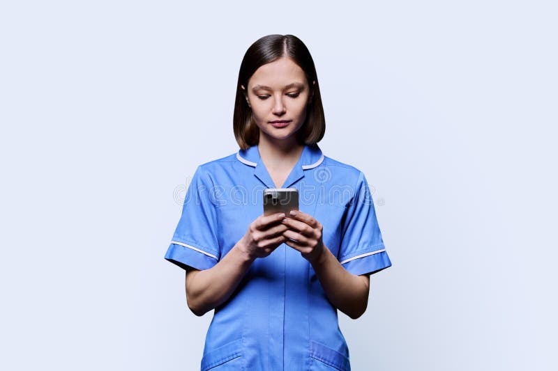 Serious young female nurse using smartphone, on white studio background. Mobile apps applications, technologies in medical services, health, professional assistance, medical care concept. Serious young female nurse using smartphone, on white studio background. Mobile apps applications, technologies in medical services, health, professional assistance, medical care concept