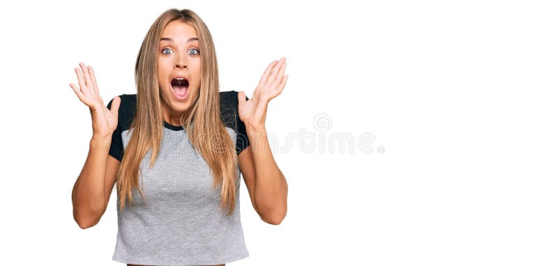νεαρή ξανθιά γυναίκα που φορούσε περιστασιακά ρούχα γιορτάζοντας την τρέλα και έκπληκτη για την επιτυχία με σηκωμένα χέρια και ανο στοκ φωτογραφία με δικαίωμα ελεύθερης χρήσης