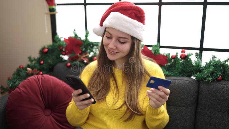 νεαρή ξανθιά γυναίκα που χρησιμοποιεί smartphone και πιστωτική κάρτα καθισμένη στον καναπέ μέχρι τη χριστουγεννιάτικη διακόσμηση σ στοκ φωτογραφία με δικαίωμα ελεύθερης χρήσης