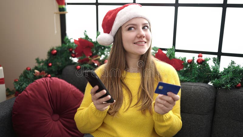 νεαρή ξανθιά γυναίκα που χρησιμοποιεί smartphone και πιστωτική κάρτα καθισμένη στον καναπέ μέχρι τη χριστουγεννιάτικη διακόσμηση σ στοκ φωτογραφία με δικαίωμα ελεύθερης χρήσης