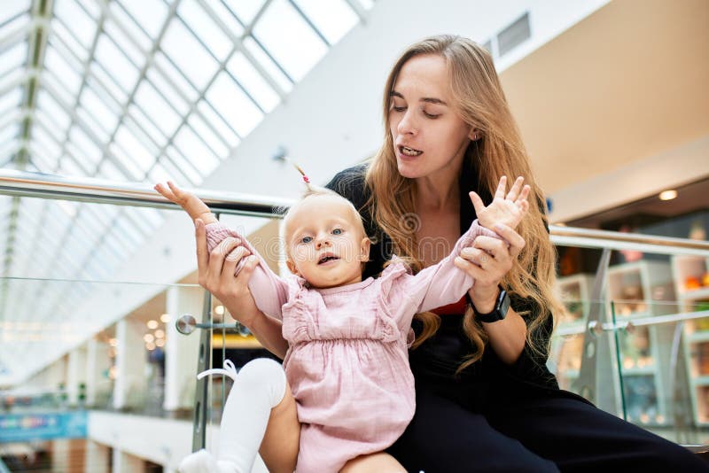 νεαρή όμορφη μητέρα με μικρό μωρό να κάθεται σε ένα παγκάκι στο εμπορικό κέντρο. μαμά και κόρη με ροζ αγκαλιά στοκ φωτογραφίες
