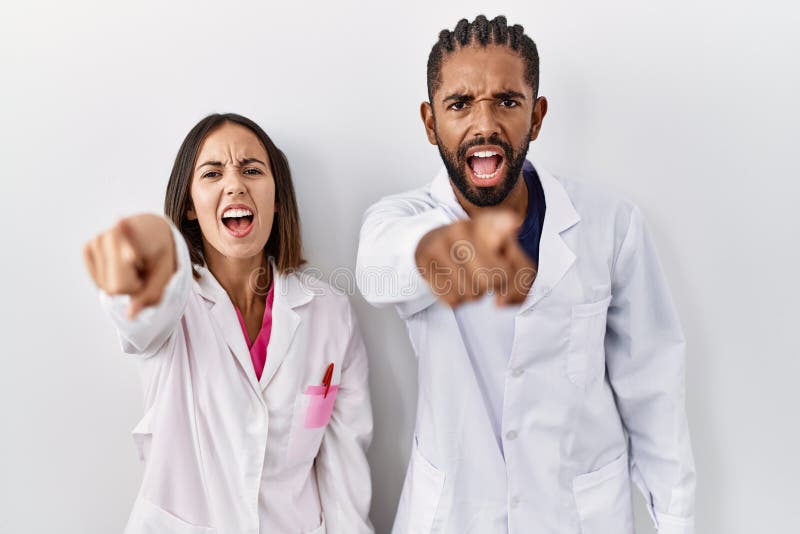 Young hispanic doctors standing over white background pointing displeased and frustrated to the camera, angry and furious with you. Young hispanic doctors standing over white background pointing displeased and frustrated to the camera, angry and furious with you