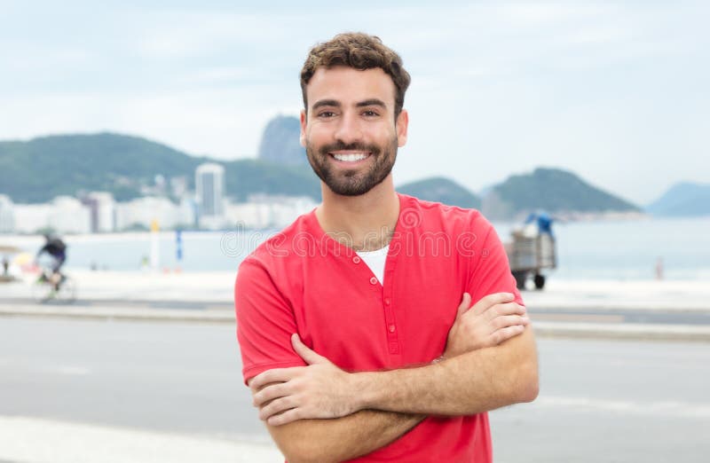 Νεαρός άνδρας με το κόκκινο πουκάμισο και γενειάδα που στέκεται στην πόλη στοκ εικόνες Νεαρός άνδρας με το κόκκινο πουκάμισο και γενειάδα που στέκεται στην πόλη στοκ εικόνες