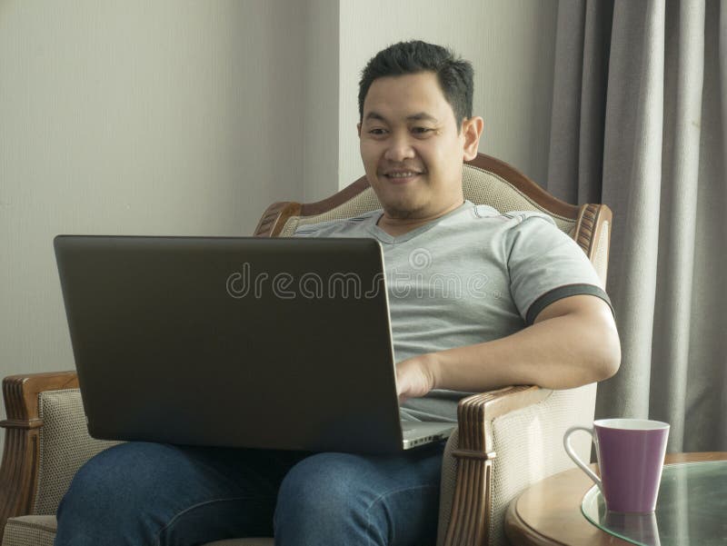 Νεαρός άνδρας που εργάζεται στο σπίτι στο lap-top του, έκφραση χαμόγελου στοκ εικόνα Νεαρός άνδρας που εργάζεται στο σπίτι στο lap-top του, έκφραση χαμόγελου στοκ εικόνα