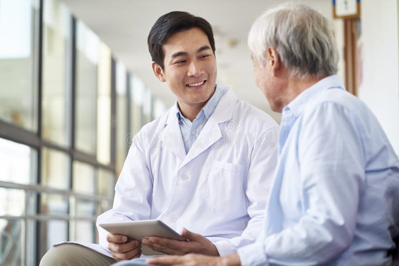 Friendly smiling young asian doctor talking and explaining test result to elderly patient in hospital. Friendly smiling young asian doctor talking and explaining test result to elderly patient in hospital