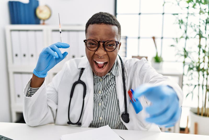 Young african doctor man holding syringe at the hospital pointing displeased and frustrated to the camera, angry and furious with you. Young african doctor man holding syringe at the hospital pointing displeased and frustrated to the camera, angry and furious with you