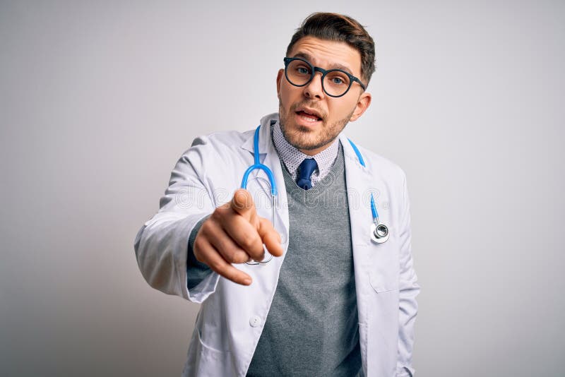 Young doctor man with blue eyes wearing medical coat and stethoscope over isolated background pointing displeased and frustrated to the camera, angry and furious with you. Young doctor man with blue eyes wearing medical coat and stethoscope over isolated background pointing displeased and frustrated to the camera, angry and furious with you