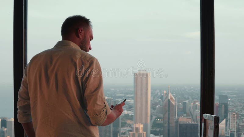 νεαρός όμορφος άνδρας έρχεται σε ένα παράθυρο στον ουρανοξύστη και κοιτάζει το πανόραμα στο κέντρο της αμερικής.