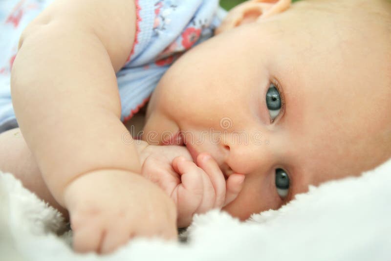 A beautidul newborn baby girl is laying down on a soft white blanket looking at the camera as she is sucking her thumb. A beautidul newborn baby girl is laying down on a soft white blanket looking at the camera as she is sucking her thumb.