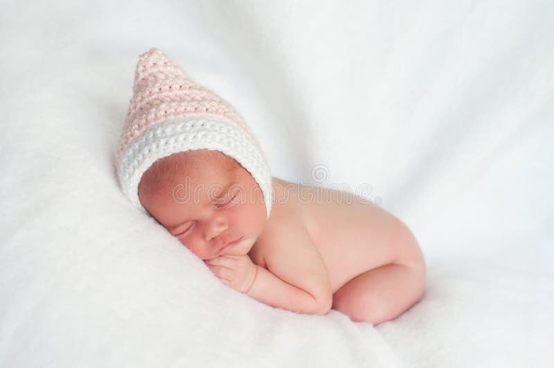 2 week old newborn girl wearing a pink, crocheted pixie hat sleeping on a white blanket. 2 week old newborn girl wearing a pink, crocheted pixie hat sleeping on a white blanket.
