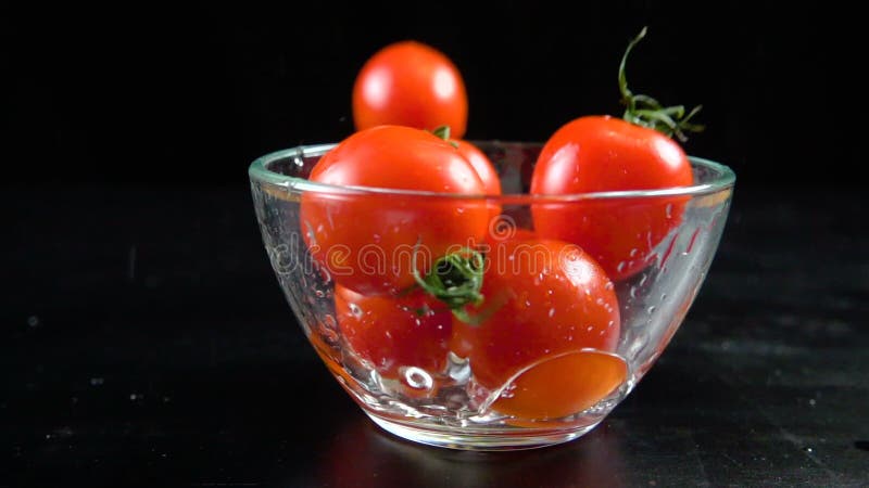 Ντομάτες κερασιών πτώσης στο κύπελλο γυαλιού, σε αργή κίνηση