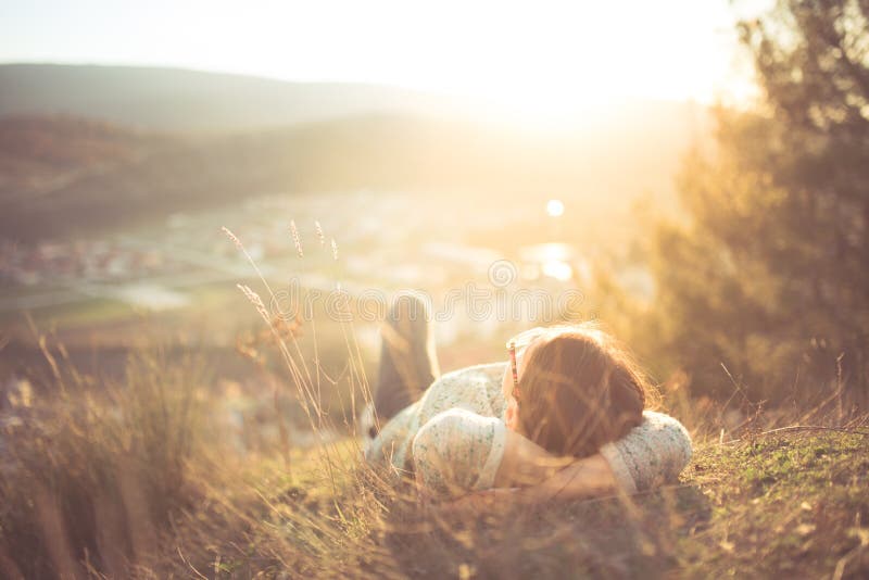 Carefree happy woman lying on green grass meadow on top of mountain edge cliff enjoying sun on her face. Enjoying nature sunset. Freedom. Enjoyment. Relaxing in mountains at sunrise. Sunshine. Daydreaming. Carefree happy woman lying on green grass meadow on top of mountain edge cliff enjoying sun on her face. Enjoying nature sunset. Freedom. Enjoyment. Relaxing in mountains at sunrise. Sunshine. Daydreaming