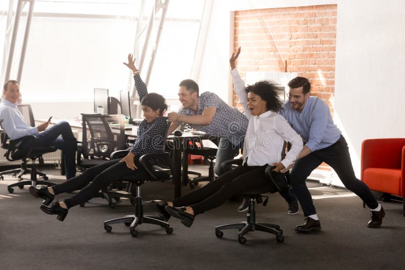 Carefree excited diverse workers having fun riding oh chairs celebrating friday together, happy employees enjoy funny competition laughing together feel great at work break, friendly office team game. Carefree excited diverse workers having fun riding oh chairs celebrating friday together, happy employees enjoy funny competition laughing together feel great at work break, friendly office team game