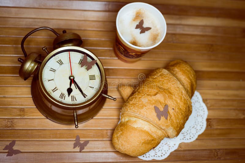 Ξυπνητήρι, ένα μίας χρήσης φλυτζάνι του espresso και. Εικόνα κινηματογραφήσεων σε πρώτο πλάνο του ξυπνητηριού, ένα μίας χρήσης φλυτζάνι του espresso και croissant ως έννοια της ζωής