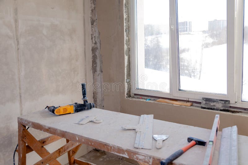Ξύλινη στάση υλικών σκαλωσιάς στο παράθυρο σε ένα μεγάλο κενό δωμάτιο, επισκευή, επικονίαση, τοίχοι ζωγραφικής, εργαλεία οικοδόμη στοκ φωτογραφίες με δικαίωμα ελεύθερης χρήσης Ξύλινη στάση υλικών σκαλωσιάς στο παράθυρο σε ένα μεγάλο κενό δωμάτιο, επισκευή, επικονίαση, τοίχοι ζωγραφικής, εργαλεία οικοδόμη στοκ φωτογραφίες με δικαίωμα ελεύθερης χρήσης