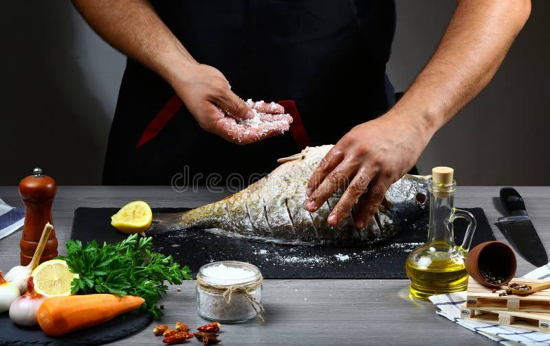 Ο αρχιμάγειρας δίνει τον κυπρίνο, το λεμόνι, τα χορτάρια και τα καρυκεύματα ψαριών μαγειρέματος σε έναν πίνακα σχιστόλιθου φρέσκι στοκ εικόνα με δικαίωμα ελεύθερης χρήσης Ο αρχιμάγειρας δίνει τον κυπρίνο, το λεμόνι, τα χορτάρια και τα καρυκεύματα ψαριών μαγειρέματος σε έναν πίνακα σχιστόλιθου φρέσκι στοκ εικόνα με δικαίωμα ελεύθερης χρήσης