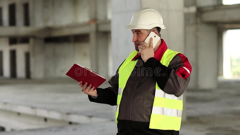 ο εργάτης μιλάει σε κινητό τηλέφωνο στην τοποθεσία του έργου απόθεμα βίντεο