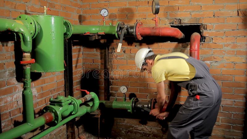 Ο εργαζόμενος στις φόρμες κλείνει τη βαλβίδα νερού Το άτομο κλείνει τη θέρμανση στο δωμάτιο λεβήτων