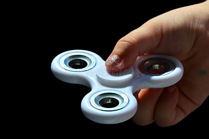 Ο λευκός fidget κλώστης κράτησε μεταξύ του αντίχειρα και του αντίχειρα χρονών του κοριτσιού τέσσερα με το διακοσμημένο καρφί, άσπ στοκ εικόνα με δικαίωμα ελεύθερης χρήσης Ο λευκός fidget κλώστης κράτησε μεταξύ του αντίχειρα και του αντίχειρα χρονών του κοριτσιού τέσσερα με το διακοσμημένο καρφί, άσπ στοκ εικόνα με δικαίωμα ελεύθερης χρήσης