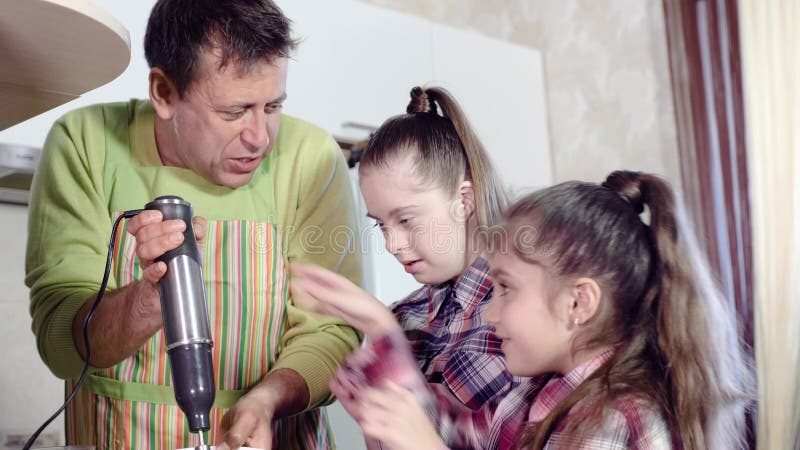 Ο εύθυμος πατέρας της οικογένειας με τις κόρες έχει τη διασκέδαση προετοιμάζοντας το γεύμα που χρησιμοποιεί έναν αναμίκτη κουζινώ