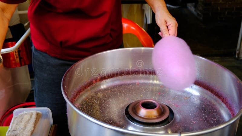 A lady is now starting to form cotton candy using a metallic machine, sugar, and skewers. A lady is now starting to form cotton candy using a metallic machine, sugar, and skewers.