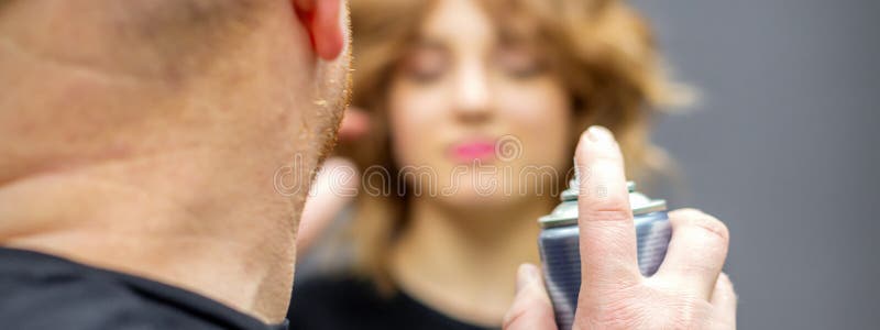 ο κομμωτής χρησιμοποιεί σπρέι για να φτιάξει το στυλ των μαλλιών της νεαρής καυκάσης στο κομμωτήριο κοντά στοκ φωτογραφίες