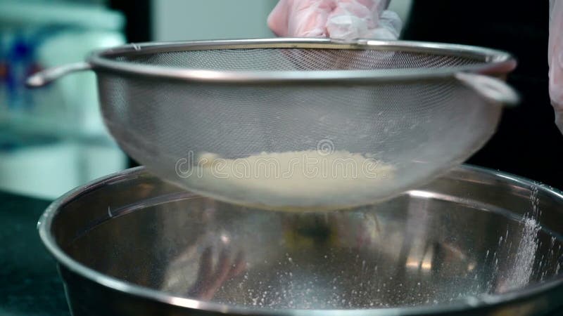Ο μάγειρας κοσκινίζει το αλεύρι μέσω του κόσκινου στον πίνακα κουζινών του εστιατορίου απόθεμα βίντεο