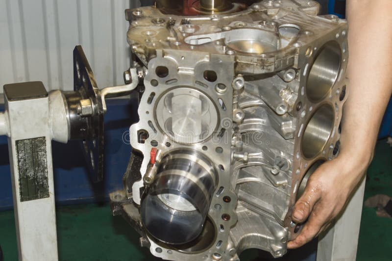 The mechanic turns over the cylinder block of the internal combustion engine which is installed on a special stand when installing the piston. The mechanic turns over the cylinder block of the internal combustion engine which is installed on a special stand when installing the piston