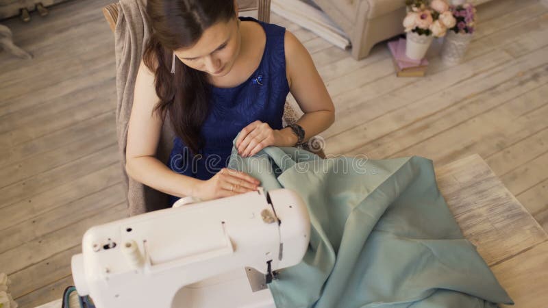 Ο νέοι σχεδιαστής ιματισμού και seamstress η γυναίκα εργάζονται με τη ράβοντας μηχανή στο στούντιο ραφτών
