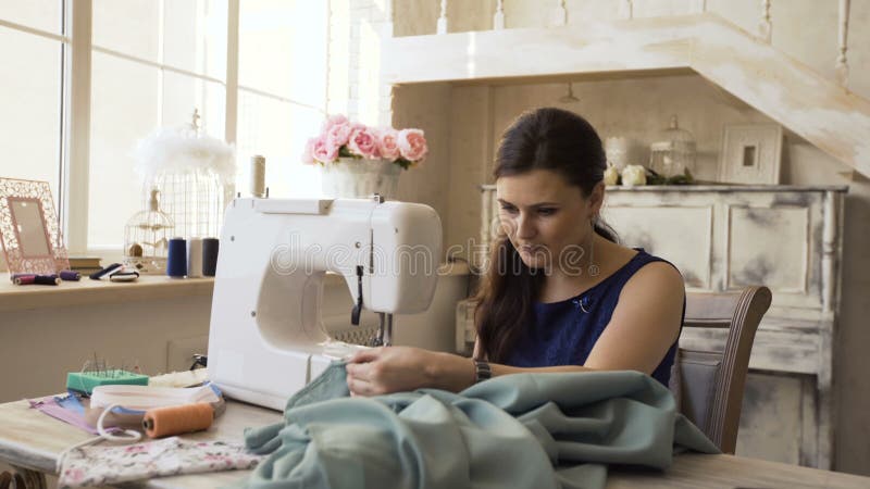 Ο νέοι σχεδιαστής ιματισμού και seamstress η γυναίκα εργάζονται με τη ράβοντας μηχανή στο στούντιο ραφτών