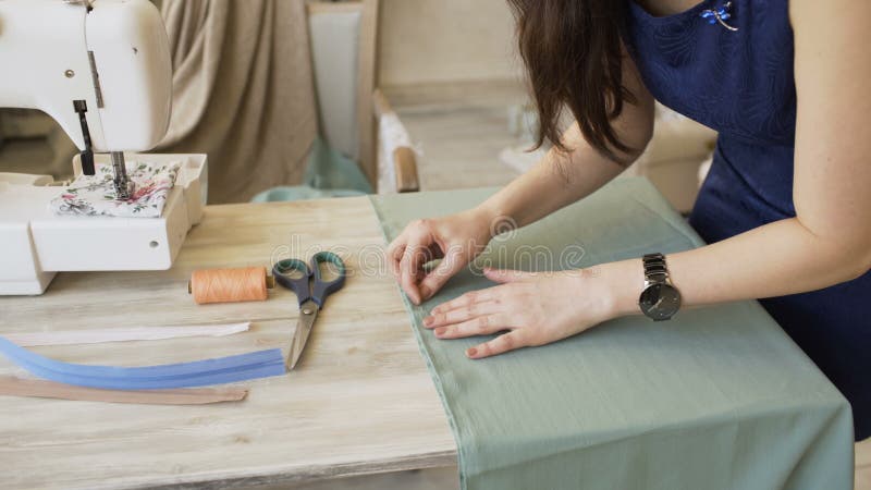 Ο νέοι σχεδιαστής ιματισμού και seamstress η γυναίκα ράβουν με μηχανή νημάτων και βελόνων τη ράβοντας πλησίον