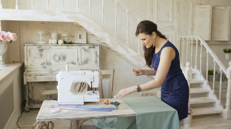 Ο νέοι σχεδιαστής ιματισμού και seamstress η γυναίκα ράβουν με μηχανή νημάτων και βελόνων τη ράβοντας πλησίον