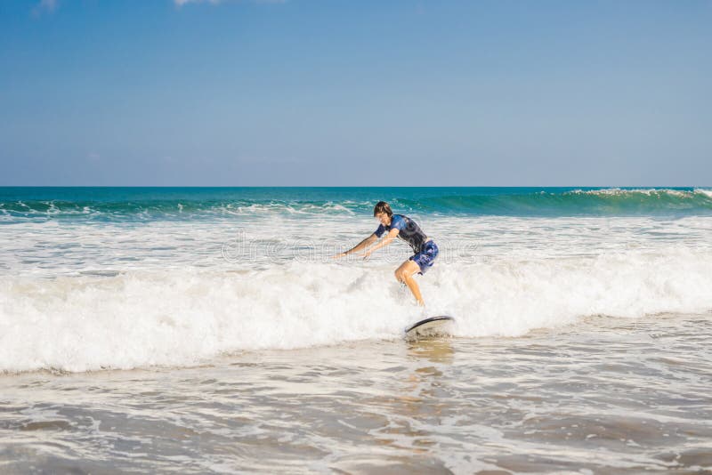 Ο νεαρός άνδρας, αρχάριος Surfer μαθαίνει να κάνει σερφ σε έναν αφρό θάλασσας στο Β στοκ φωτογραφία με δικαίωμα ελεύθερης χρήσης Ο νεαρός άνδρας, αρχάριος Surfer μαθαίνει να κάνει σερφ σε έναν αφρό θάλασσας στο Β στοκ φωτογραφία με δικαίωμα ελεύθερης χρήσης