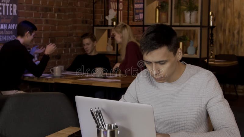 Ο νεαρός άνδρας εργάζεται στο lap-top του στο μοντέρνο καφέ απόθεμα βίντεο