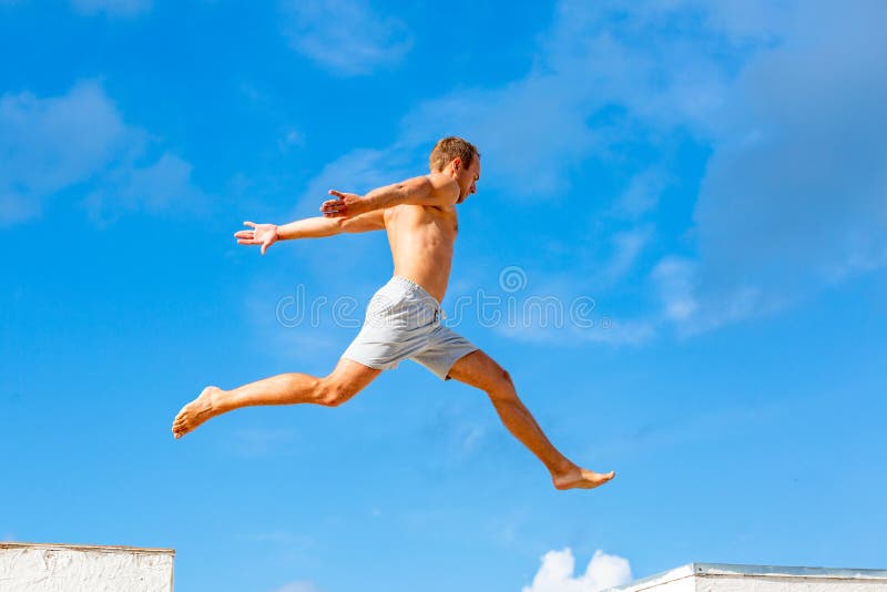 Ο νεαρός άνδρας που κάνει parkour πηδά στο υπόβαθρο μπλε ουρανού την ηλιόλουστη θερινή ημέρα στοκ εικόνες