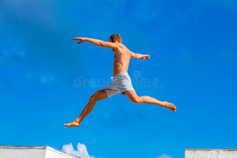 Ο νεαρός άνδρας που κάνει parkour πηδά στο υπόβαθρο μπλε ουρανού την ηλιόλουστη θερινή ημέρα στοκ εικόνες
