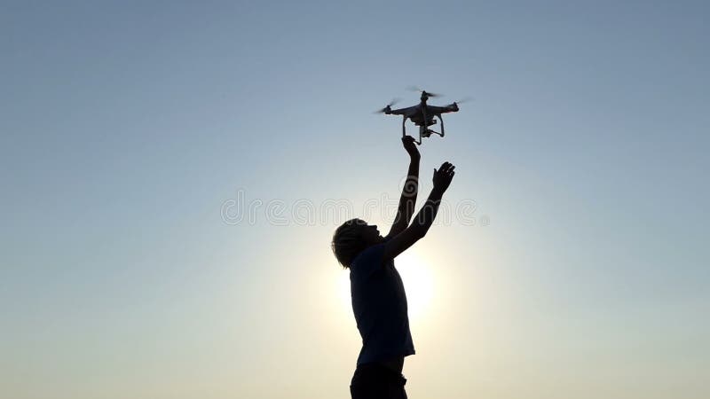 Ο νεαρός άνδρας προσπαθεί να αγγίξει έναν πετώντας κηφήνα στο ηλιοβασίλεμα στην slo-Mo