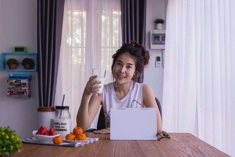 Ο πίνακας προγευμάτων με τη νέα ασιατική γυναίκα πίνει κάποιο γάλα στο καθιστικό