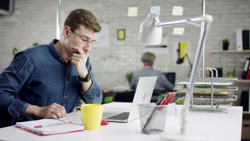 Ο παραγωγικός συγκεντρωμένος επιχειρηματίας που κλίνει την πίσω εργασία γραφείων λήξης για το lap-top, αποτελεσματικός διευθυντής