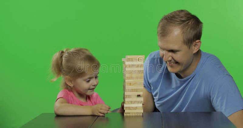 Ο πατέρας και η κόρη παίζουν το jenga Λίγο παιδί τραβά τους ξύλινους φραγμούς από τον πύργο στοκ εικόνα με δικαίωμα ελεύθερης χρήσης Ο πατέρας και η κόρη παίζουν το jenga Λίγο παιδί τραβά τους ξύλινους φραγμούς από τον πύργο στοκ εικόνα με δικαίωμα ελεύθερης χρήσης