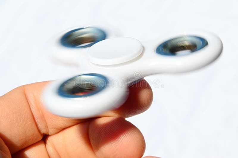 Ο περιστρεφόμενος λευκός fidget κλώστης κράτησε μεταξύ του αντίχειρα και του αντίχειρα του ενήλικου αρσενικού προσώπου, χλωμό υπό στοκ εικόνες Ο περιστρεφόμενος λευκός fidget κλώστης κράτησε μεταξύ του αντίχειρα και του αντίχειρα του ενήλικου αρσενικού προσώπου, χλωμό υπό στοκ εικόνες