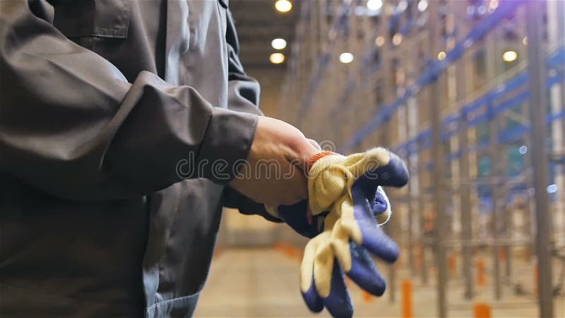 Ο σε αργή κίνηση εργαζόμενος κινηματογραφήσεων σε πρώτο πλάνο βάζει στα γάντια στην αποθήκη εμπορευμάτων απόθεμα βίντεο