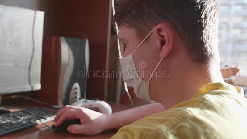 ο τύπος παίζει στον υπολογιστή με προστατευτική μάσκα και μένει στο σπίτι του με αυτοαπομόνωση. πρόληψη και προστασία της υγείας