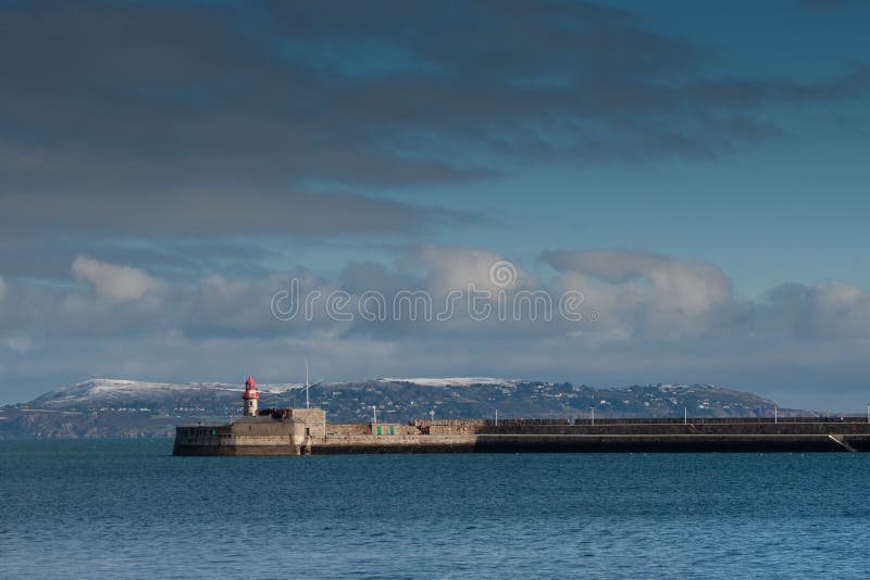 Ο φάρος στο dun laoghaire ελλιμενίζει με το λόφο της κάλυψης Howth από το χιόνι, Ιρλανδία στοκ εικόνες Ο φάρος στο dun laoghaire ελλιμενίζει με το λόφο της κάλυψης Howth από το χιόνι, Ιρλανδία στοκ εικόνες