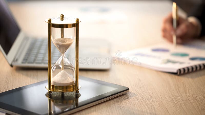 Ο χρόνος τρέχει στην κλεψύδρα, θηλυκός διευθυντής που ελέγχει τις γραφικές παραστάσεις στο γραφείο γραφείων στοκ εικόνες με δικαίωμα ελεύθερης χρήσης Ο χρόνος τρέχει στην κλεψύδρα, θηλυκός διευθυντής που ελέγχει τις γραφικές παραστάσεις στο γραφείο γραφείων στοκ εικόνες με δικαίωμα ελεύθερης χρήσης